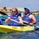 2 couples in kayaks near a beach with buildings